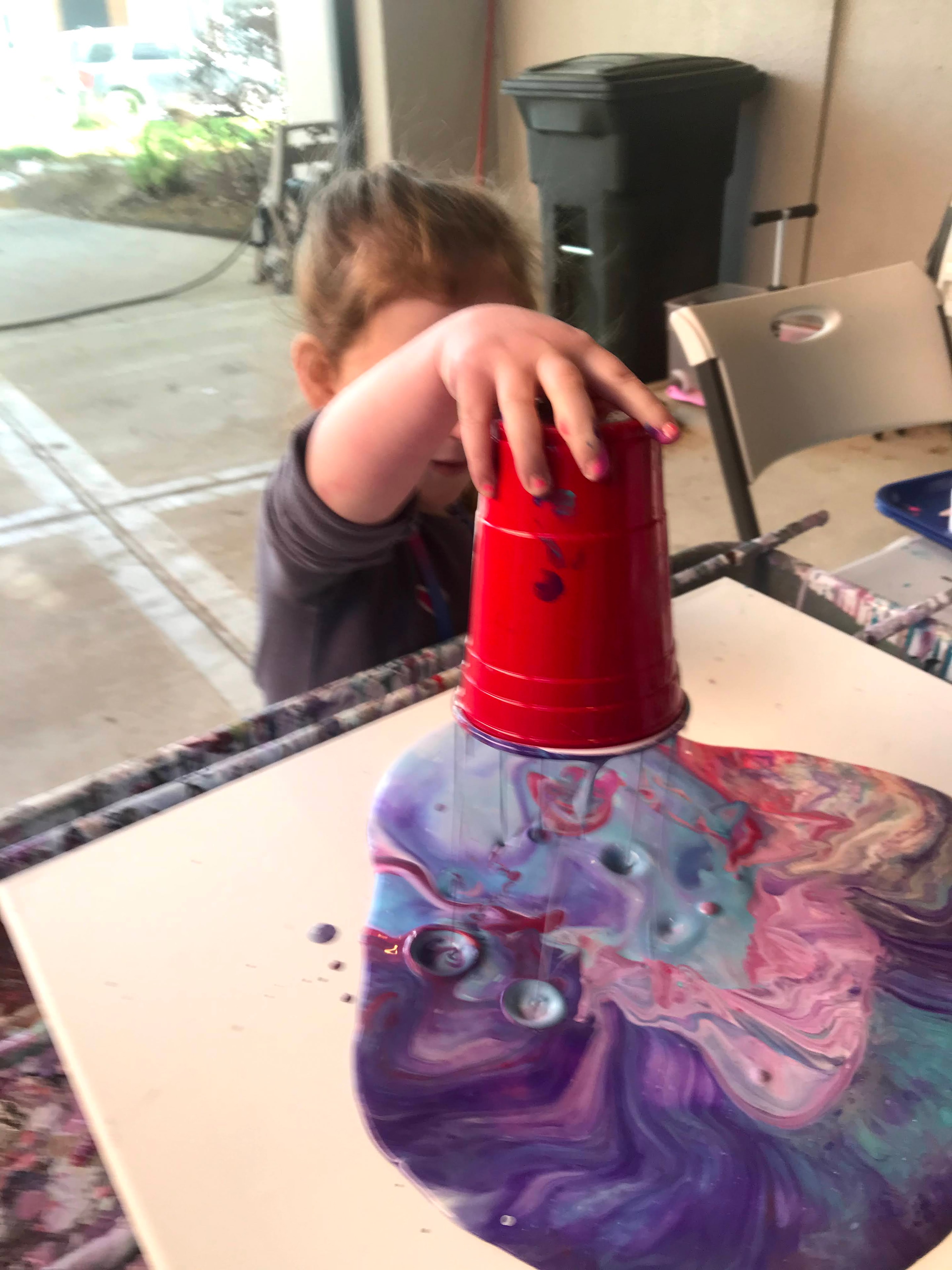 Child doing a flip cup pour painting with a red cup